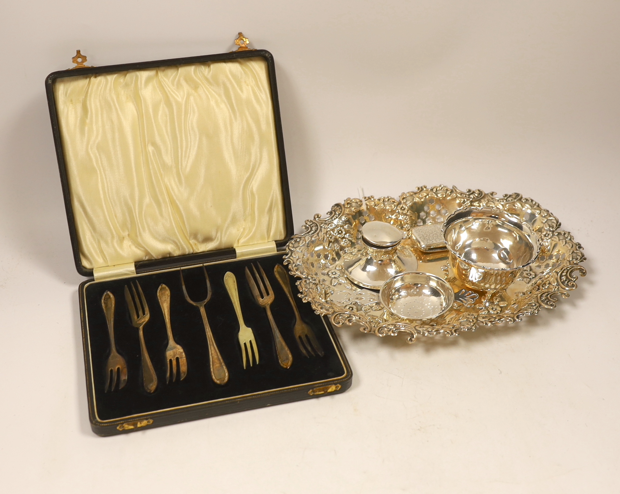 A George V pierced silver oval dish, London, 1914, 26.4cm, together with a small silver bowl, silver mounted inkstand, silver vesta case, silver tea strainer and a cased set of plated pastry forks.